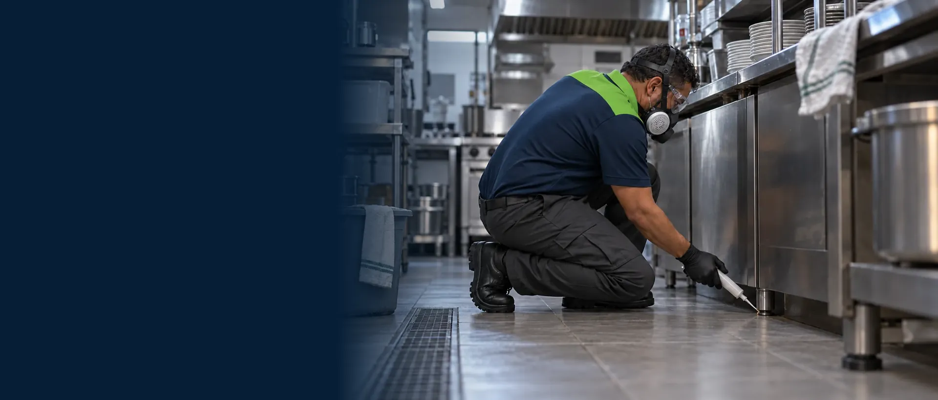 Dedetizador de uniforme e máscara aplicando gel embaixo da bancada de inox de uma cozinha comercial